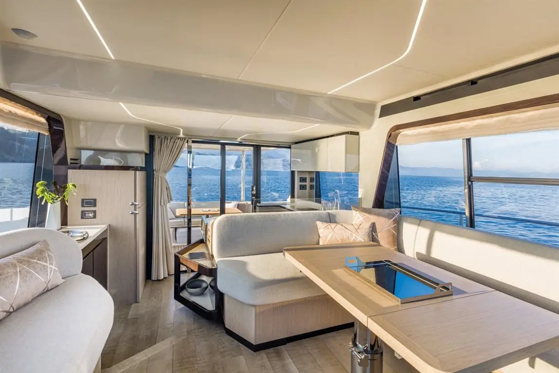 Interior of a modern yacht featuring a stylish lounge area, kitchenette, and panoramic windows overlooking the ocean.